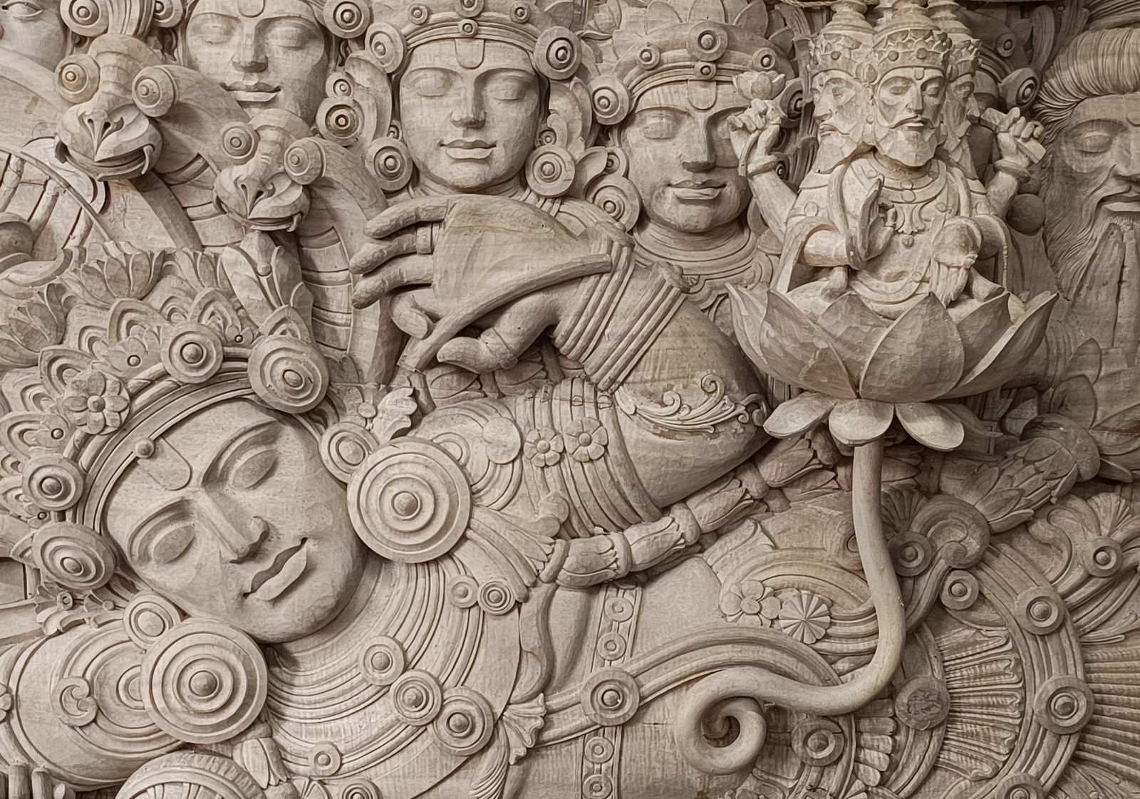 Detail of the unfinished kumbil-wood carving: Vishnu asleep on the serpent Adisesha, with Brahma seated on the lotus that rises from his navel, and the faces of the Dikpalakas behind.