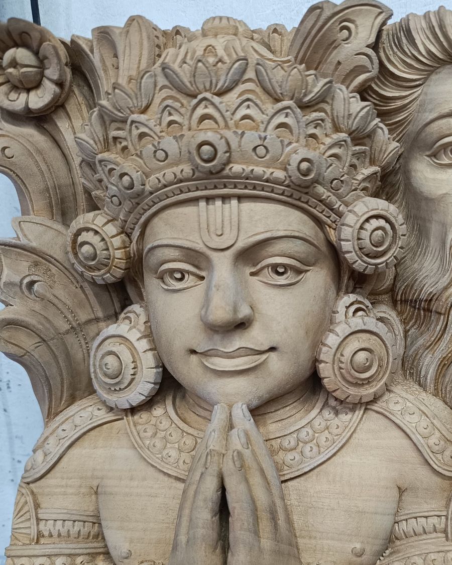 Indra, carved in kumbil wood: jewelled crown, Vaishnava mark on the forehead, hands joined in namaskara, with a gentle smile.